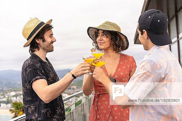 Drei glückliche Freunde stoßen im Sommer auf einer Terrasse mit Cocktails an