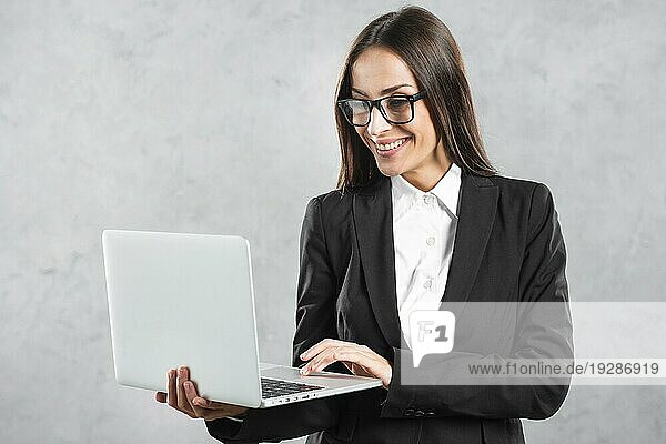 Lächelnde Geschäftsfrau sucht Laptop ihre Hand gegen Betonwand