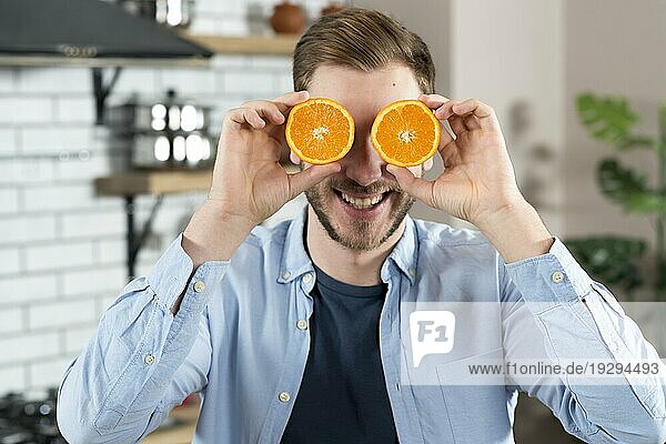 Junger Mann macht sich einen Spaß mit zwei Orangenscheiben zu Hause