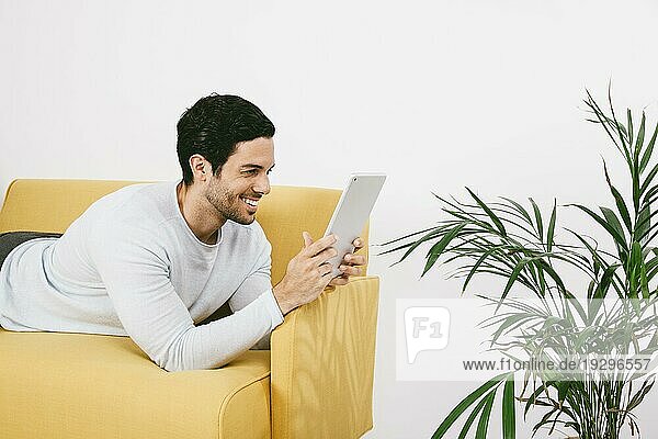 Glücklicher junger Mann auf dem Sofa mit Tablet