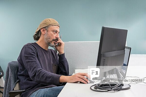 Moderner und stilvoller reifer Mann  der mit dem Telefon spricht  während er einen Computer in einer Arbeitsgruppe benutzt