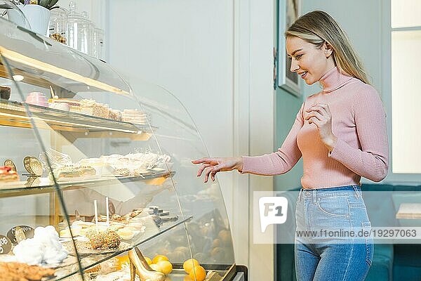 Lächelnde junge Frau  die einen Kuchen auswählt  vor einer Glasvitrine stehend