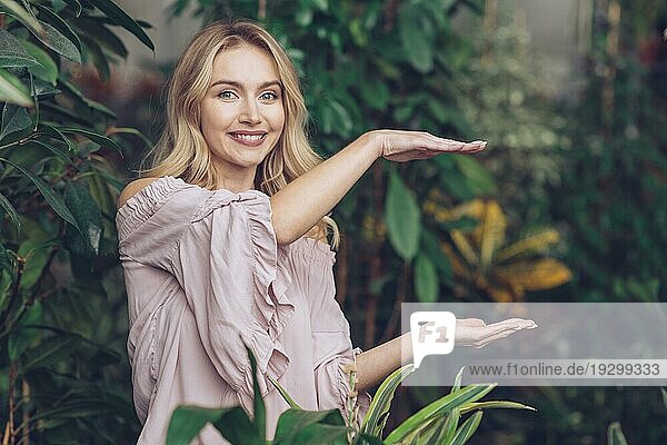 Lächelnd schöne junge Frau zeigt etwas Palmen ihre Hände Garten