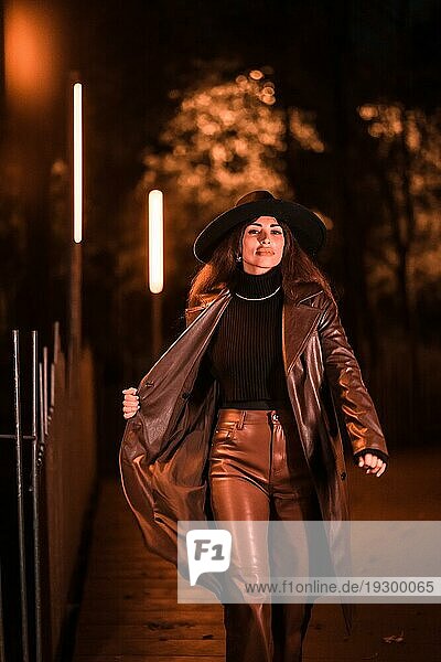 Kaukasisches brünettes Mädchen mit Hut geht nachts in einem Park spazieren. Winterabendmode  vertikales Foto