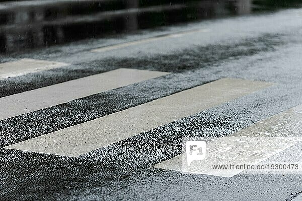 Detailaufnahme eines Zebrastreifens für Fußgänger auf nassem Straßenbelag an einem regnerischen Tag