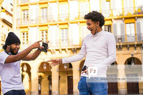 Lifestyle  zwei schwarze Latino Freunde  die sehr glücklich sind  sich lange Zeit später auf der Straße zu treffen. Junge mit Afrohaar und Junge mit Hut und Kopfhörer