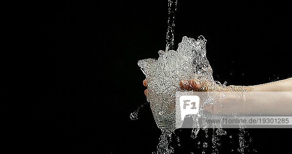 Frauenhände und fließendes Wasser im Glas auf schwarzem Hintergrund