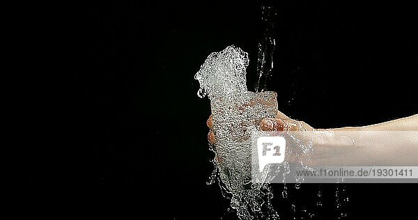 Frauenhände und fließendes Wasser im Glas auf schwarzem Hintergrund