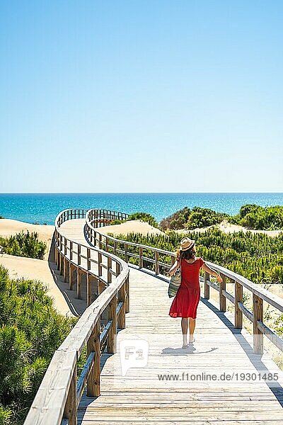 Mädchen mit rotem Kleid auf dem Holzweg zum Playa Moncayo in Guardamar del Segura bei Torrevieja  Alicante. Gemeinschaft von Valencia. Spanien  Urlaub am Mittelmeer