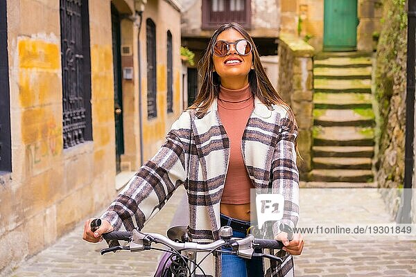 Hübsche lateinische Frau mit Sonnenbrille macht Fahrrad Sightseeing in der Stadt durch die Altstadt. Öko Tourismus im Frühjahr im Urlaub  Modell lächelnd