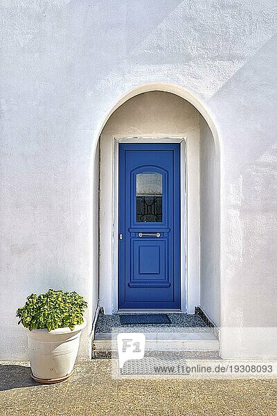 Traditionelle blaue Tür und weiß getünchte Wände des griechischen Hauseingangs und Blumentopf mit reichem Laub vor der Tür an einem sonnigen Sommertag. Heiße Sommertage  griechisches Design  Lebensstil auf einer Mittelmeerinsel  ikonische Aussicht  Milos  Griechenland  Europa