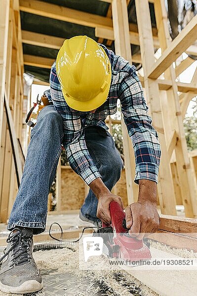 Bauarbeiter mit Schutzhelm schleift ein Holzstück ab
