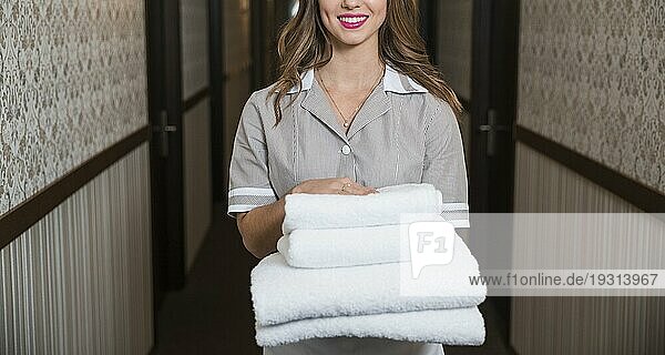 Porträt glückliches junges Dienstmädchen stehend Korridor hält gefaltete weiche Handtücher