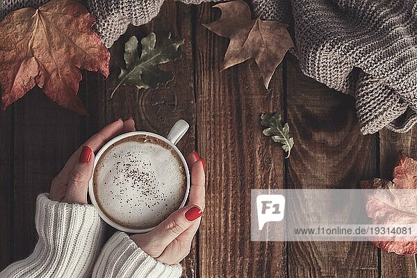 Weibliche Hände halten heißen Kaffee Cappucino  Decke und Herbstblätter auf alten hölzernen Hintergrund. Vintage Tonning. Herbst entspannen Konzept