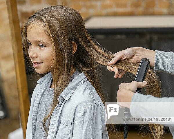 Kleines Mädchen  das von einer Kosmetikerin die Haare geglättet bekommt