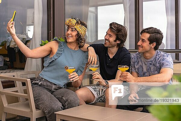 Drei stilvolle und moderne Freundinnen machen ein Selfie im Urlaub und feiern mit Cocktails