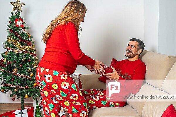 Junges Paar sitzt neben dem Weihnachtsbaum  sehr glücklich Freund mit Weihnachtsgeschenk