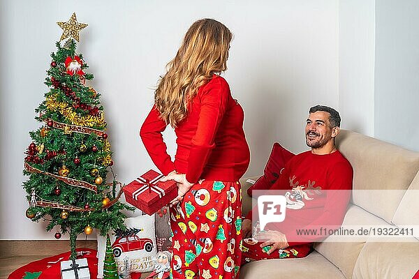Junges Paar sitzt am Weihnachtsbaum  Freundin gibt Freund ein Weihnachtsgeschenk