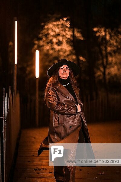 Kaukasisches brünettes Mädchen mit Hut geht nachts in einem Park spazieren. Winter Abendmode