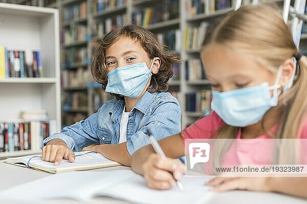 Kinder machen Hausaufgaben und tragen dabei medizinische Masken