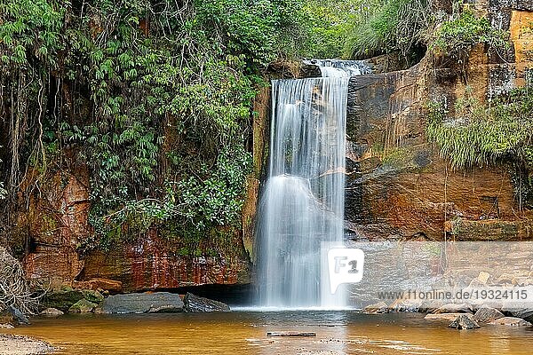 Idyllischer Wasserfall mit Wasserbewegungsunschärfe und üppiger Vegetation  rote Felsformationen  Chapada dos Guimarães  Wasserfall mit Wasserbewegungsunschärfe und üppiger Vegetation  Mato Großo  Brasilien  Südamerika