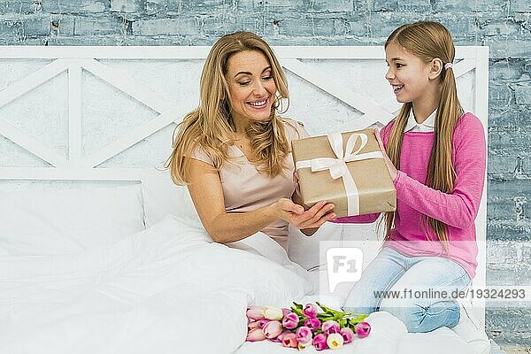 Tochter gibt Geschenkbox Mutter Bett