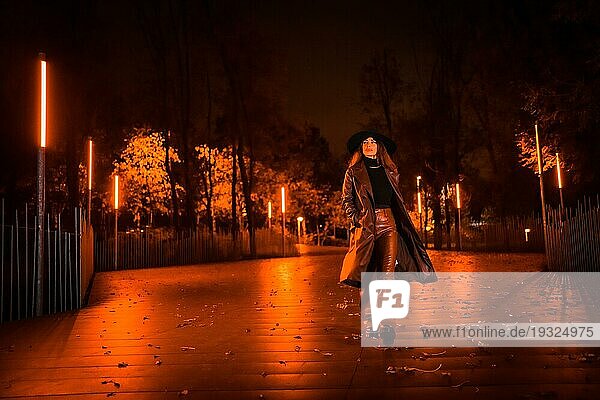 Mädchen mit Hut geht in einer Winternacht ruhig durch einen Park. Genießt die Einsamkeit der Nacht in einer modischen Pose