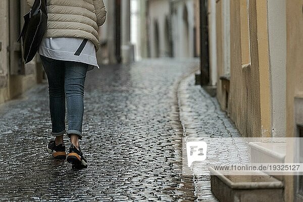 Unterer Körperteil einer nicht erkennbaren Frau  die durch eine verregnete Straße in einer alten  schmalen Schusterstraße mit Kopfsteinpflaster läuft
