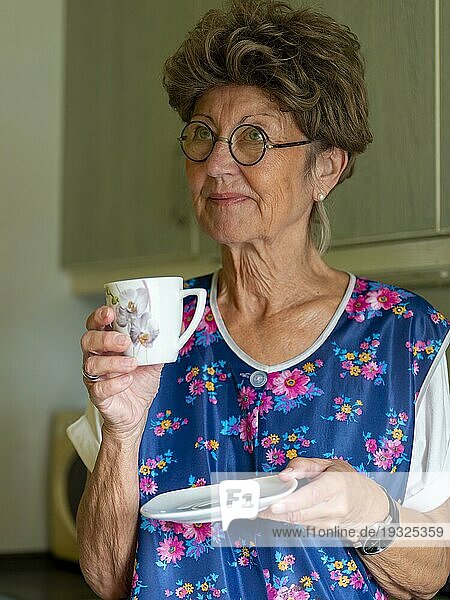 Oma mit alter Kittelschürze, Brille und Perücke in der Küche, hält