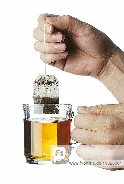 Hand  die einen gebrauchten Teebeutel aus einem durchsichtigen Teebecher hebt