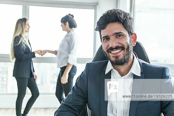 Porträt lächelnder Geschäftsmann vor Frauen beim Händeschütteln