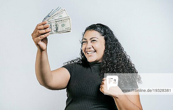 Aufgeregtes lateinamerikanisches Mädchen  das einen Dollar in bar hält  isoliert. Siegreiche junge Frau hält Geld feiern isoliert