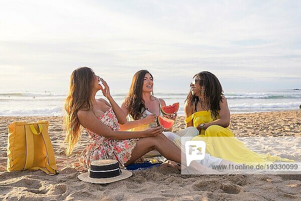 Idyllisches Sommerpicknick von drei multiethnischen Freunden  die gemeinsam am Strand Wassermelone essen