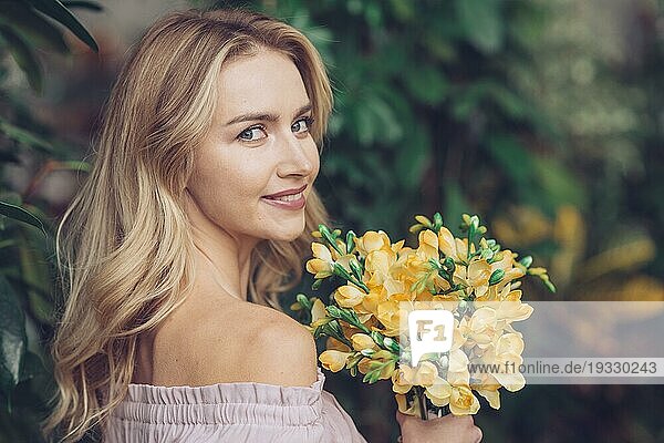 Hübsche junge Frau schaut in die Kamera und hält schöne gelbe Blumen
