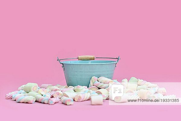 Leerer blauer Eimer umgeben von Marshmallowbonbons vor rosa Hintergrund