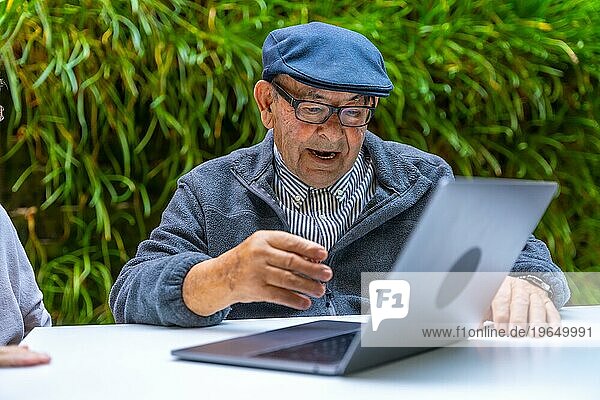 Alter Mann im Ruhestand benutzt Laptop im Garten eines Pflegeheims