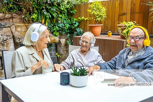 Glückliche ältere Menschen  die im Garten eines Pflegeheims mit Kopfhörern Musik genießen