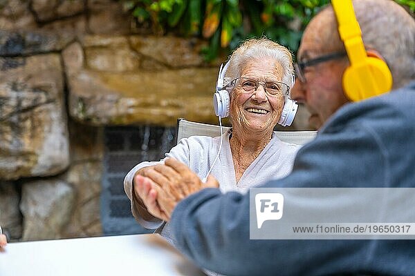 Glückliche ältere Menschen  die Kopfhörer benutzen und lächelnd in einem Garten in einer geriatrischen Einrichtung sitzen