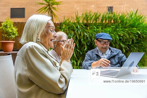 Ältere Menschen lächeln und haben Spaß bei der Benutzung eines Laptops in einer geriatrischen Einrichtung