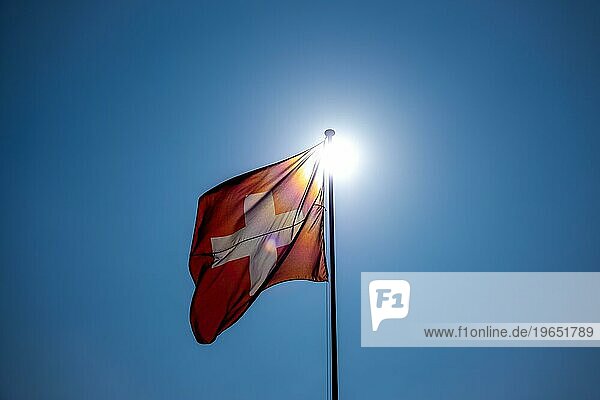 Schöne Schweizer Flagge gegen blauen klaren Himmel und die Sonne in einem windigen Tag in der Schweiz