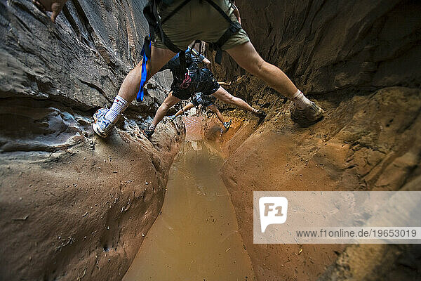 Three people stemming between two walls above water in slot canyon  Utah.
