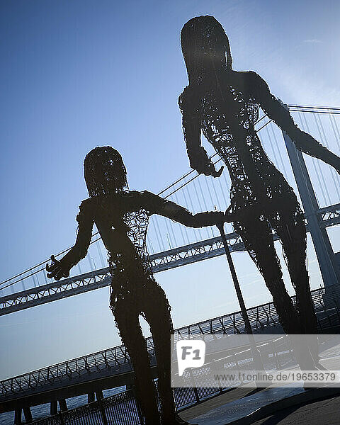 Metal sculpture of two people with a bridge in the background.