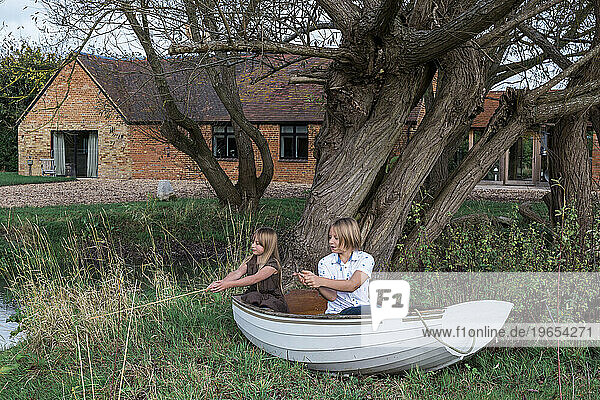 Jungen und Mädchen spielen im Fischerboot an Land und angeln im Teich am Haus.