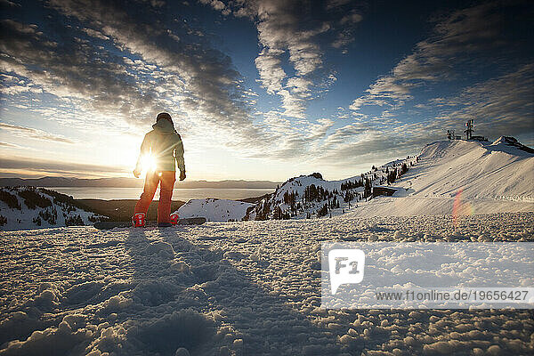 One female snowboarder at the top of a mountain at sunrise.
