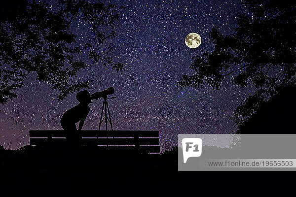 Boy at night  gazing at stars and full moon through a telescope.