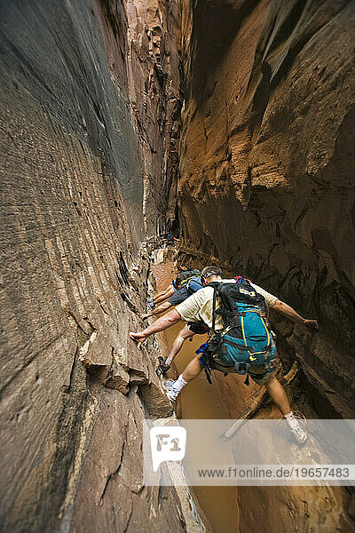 Three people stemming between two walls above water in slot canyon  Utah.