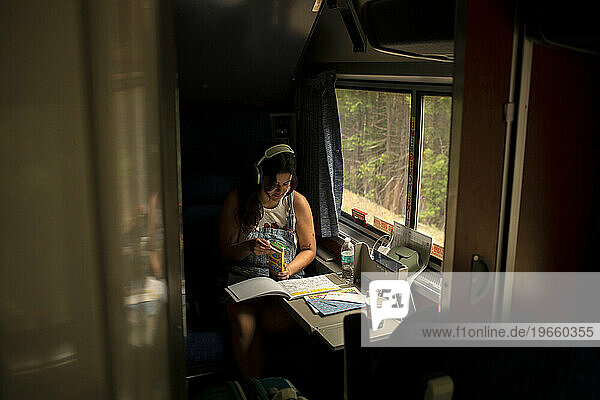 Young woman riding passenger train with coloring book