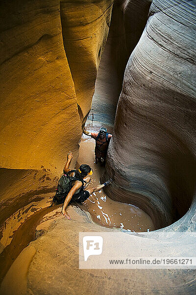 A woman down climbing into pool with man in pool in sculpted slot canyon  Utah.