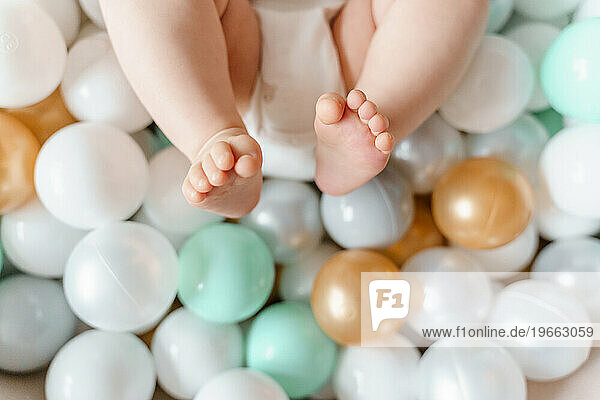Naked legs of a baby lying in a pool with balls