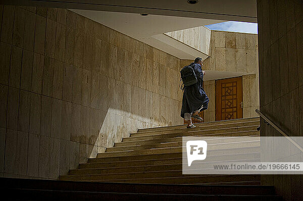 A man in traditional Middle Eastern dress walks up the stairs of a grand mosque.